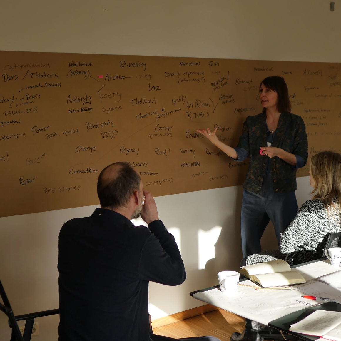 Claire speaking and showing a board with many words, people around paying attention.