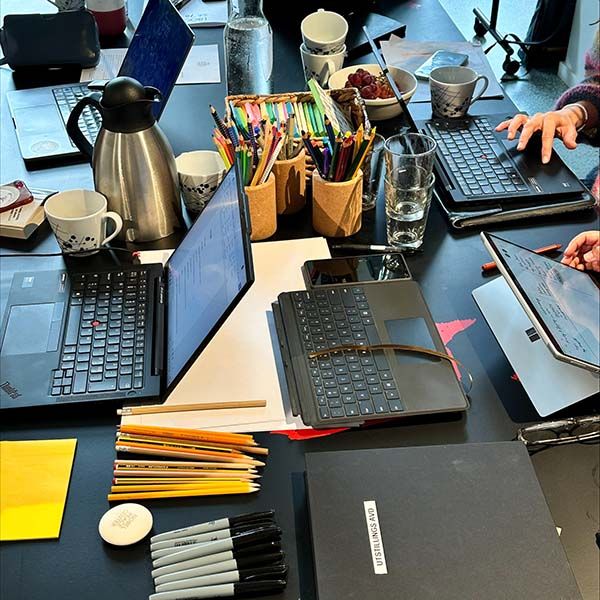 people working on a table with laptops, pens and notebooks.