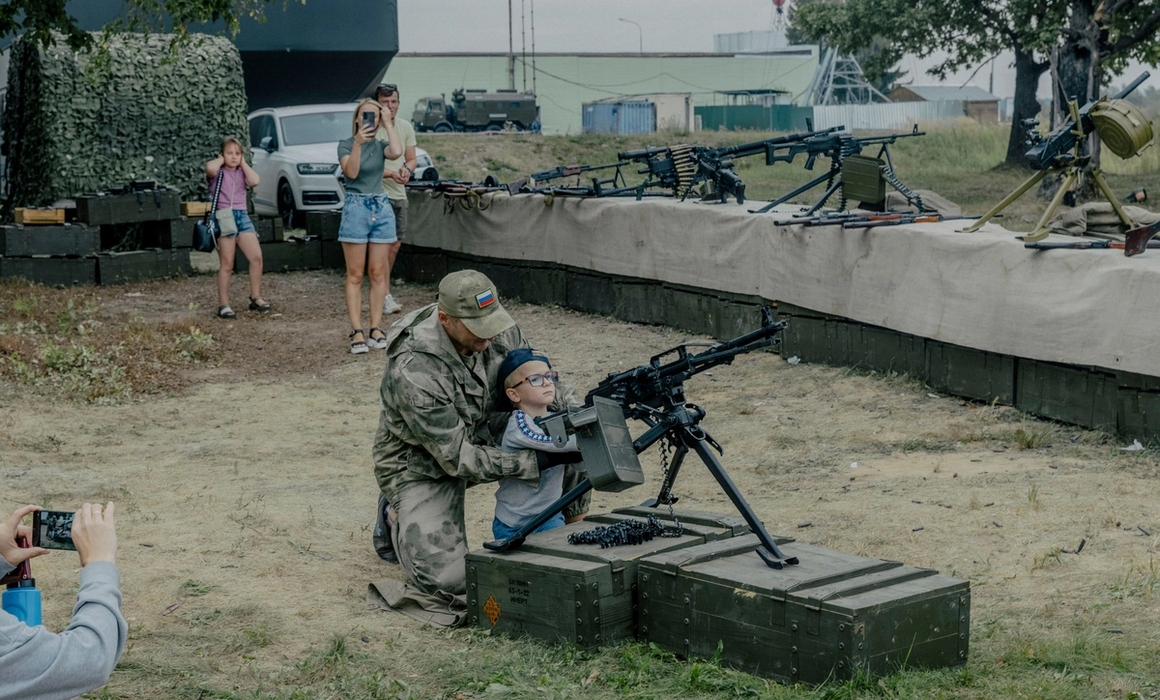 A boy being shown how to use a machine weapon.
