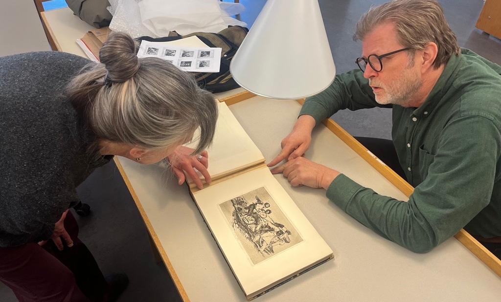 Two people looking into a book with goya illustrations