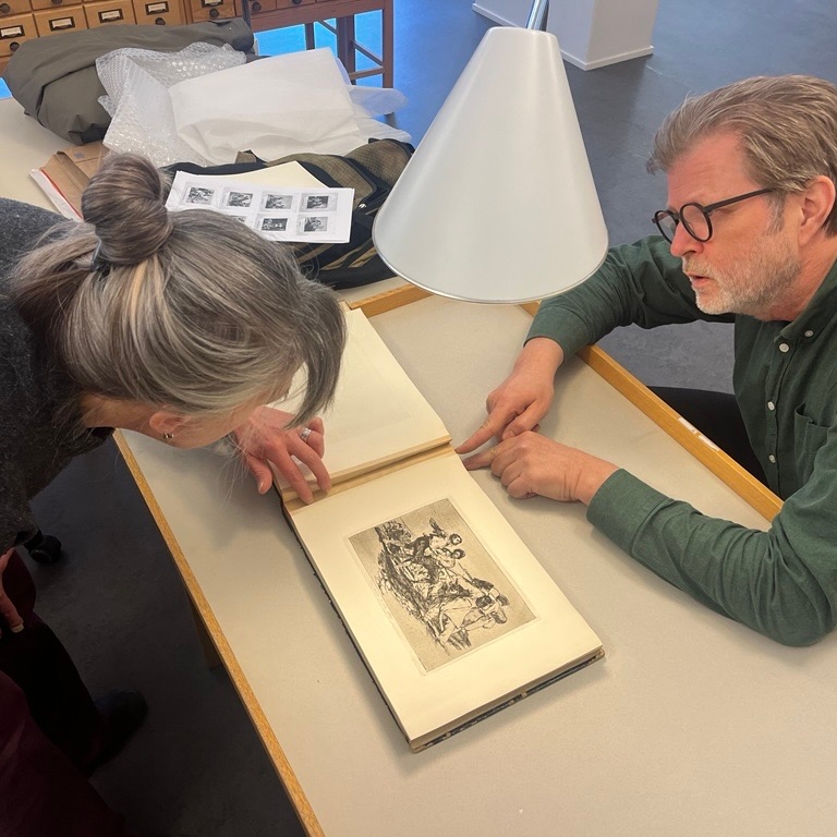 Two people looking into a book with goya illustrations