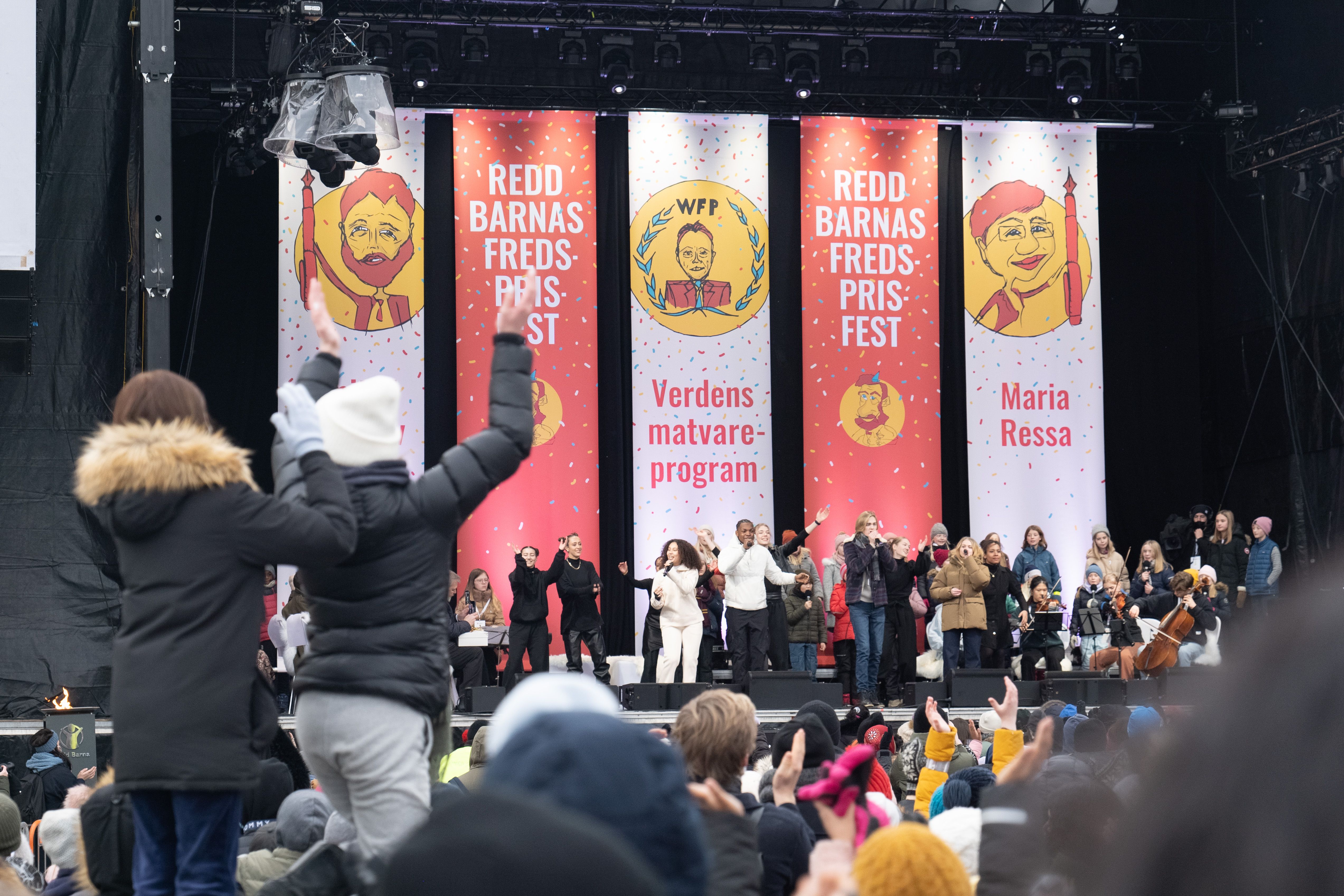 A stage full of people and a big crown clapping in front.