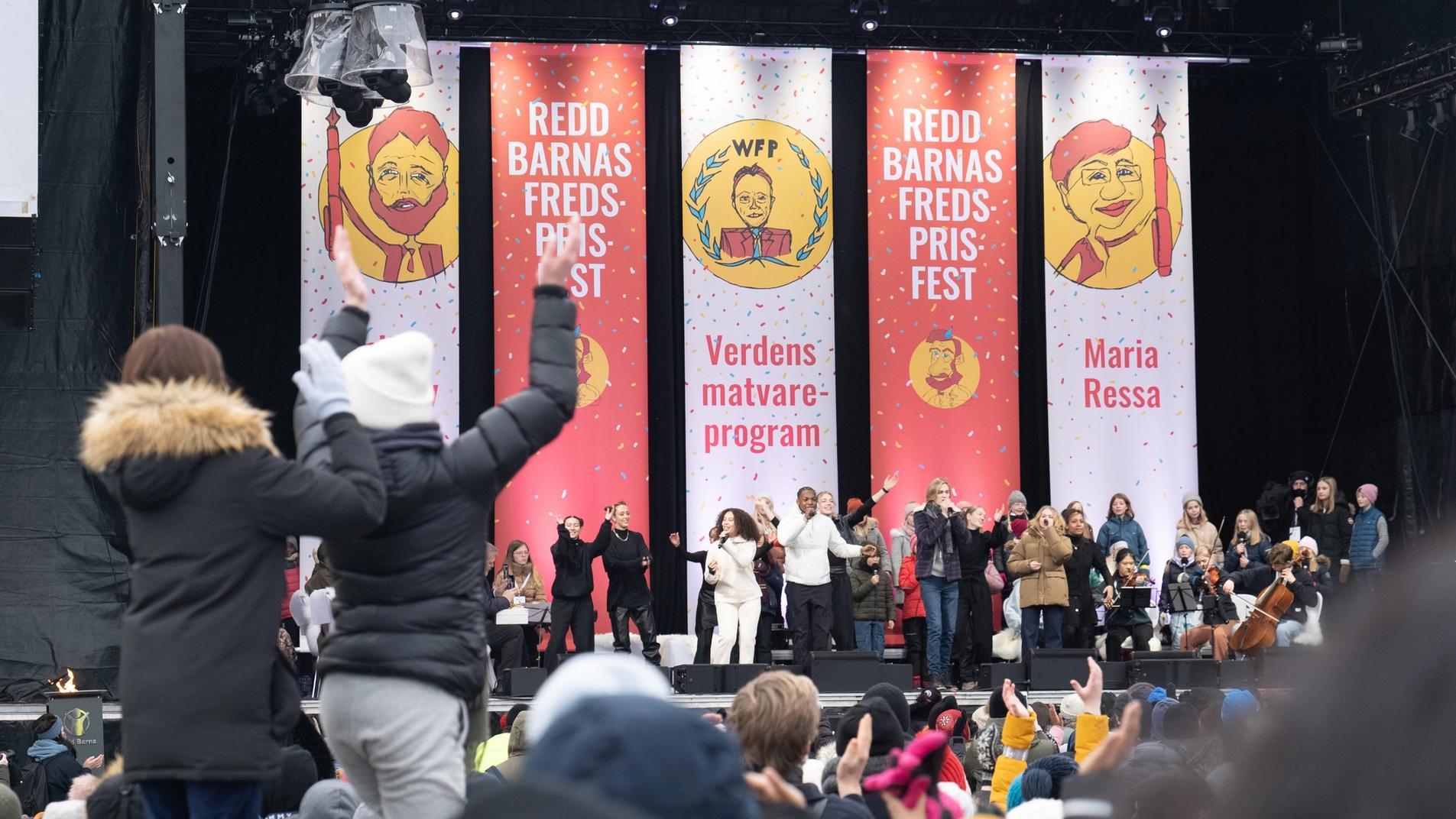 A stage full of people and a big crown clapping in front.