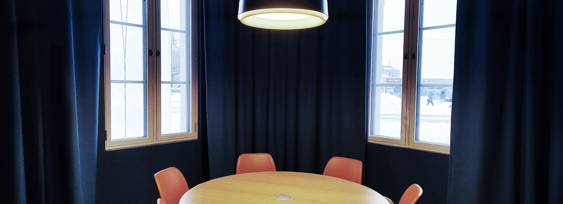 The meeting room Alfred, with 6 chairs surrounding a round table. The room is dark blue with dark blue modern curtains open to big light windows.