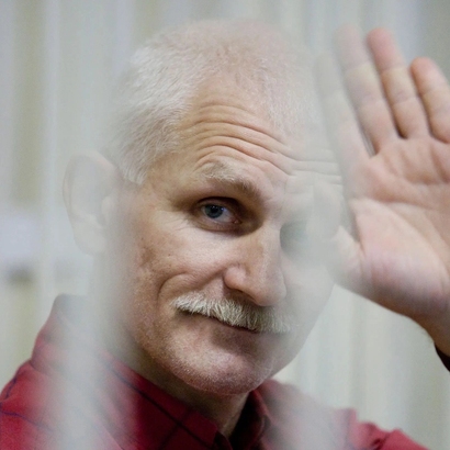Showing Ales Bialiatski behind bars, waving to the photographer