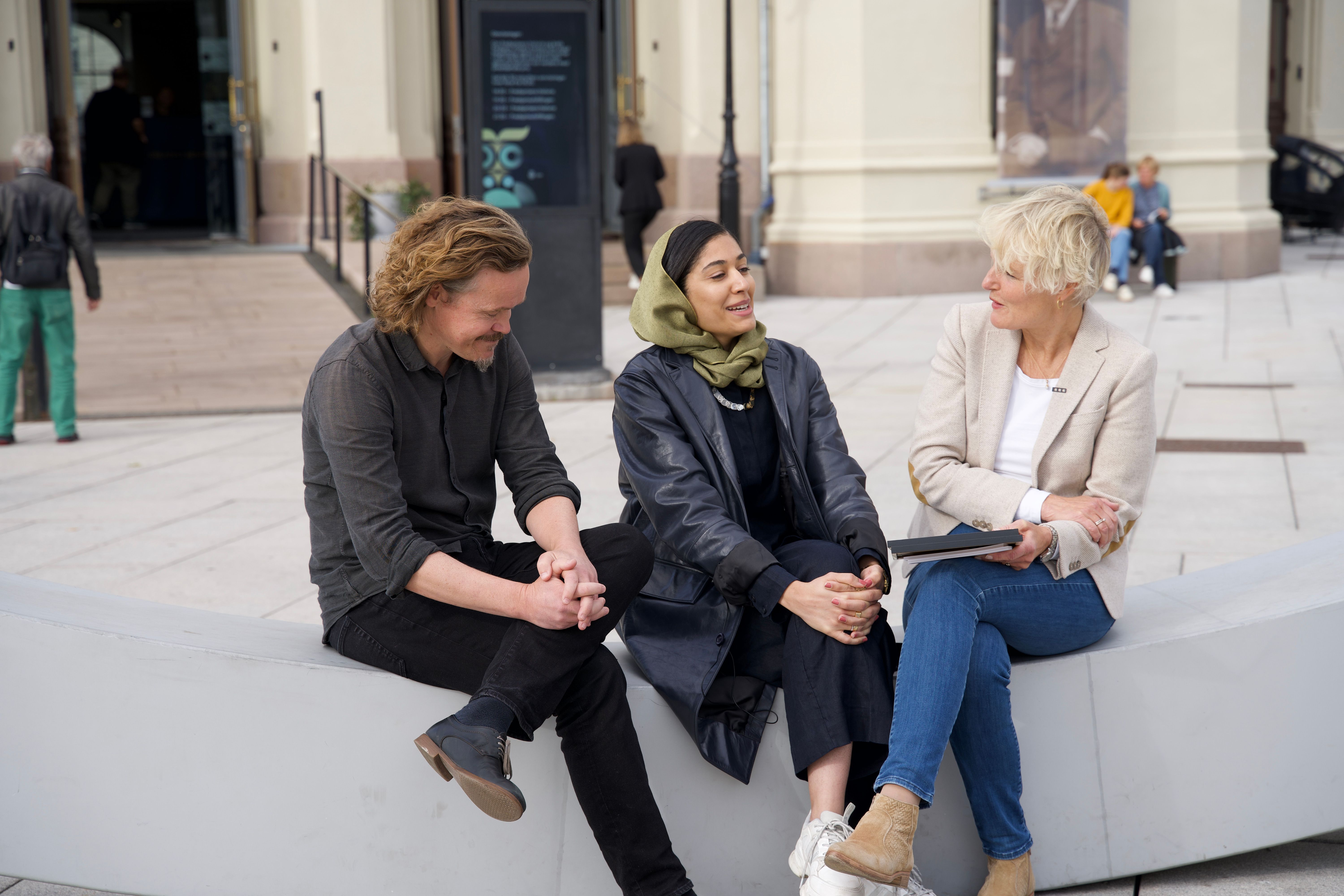 Three people sitting on a bench and talking
