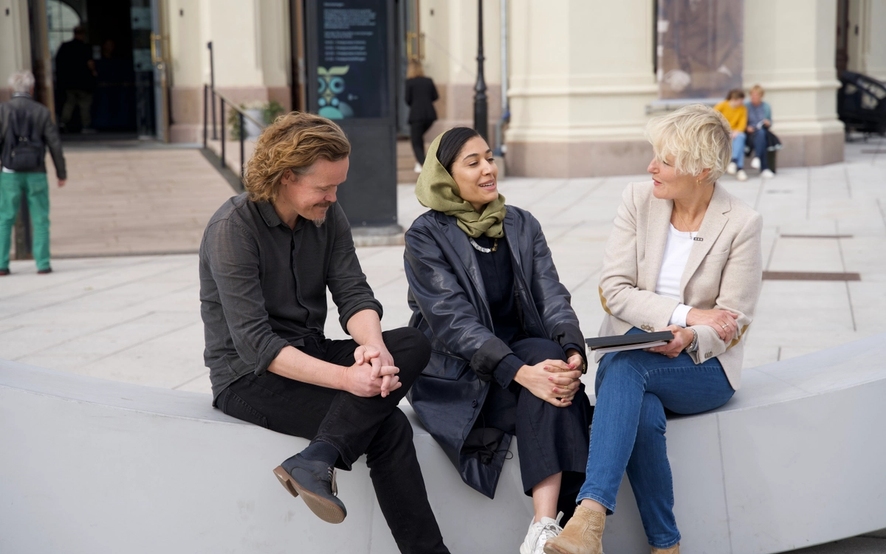 Three people sitting on a bench and talking