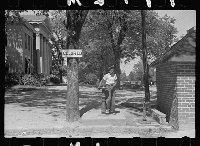 A boy in the 50s by a drinking fountain with the sign "colored"