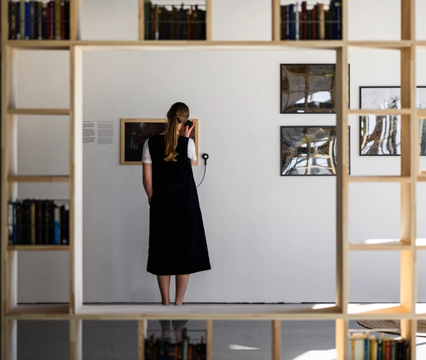 Fra utstillingen, en person som lytter til et lydspor og en bokhylle med bøker.