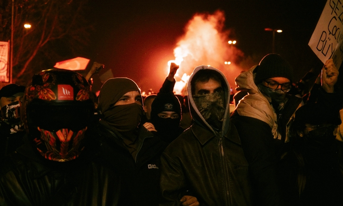 demonstrasjon, flammer i bakgrunnen, menn med masker foran ansiktet-