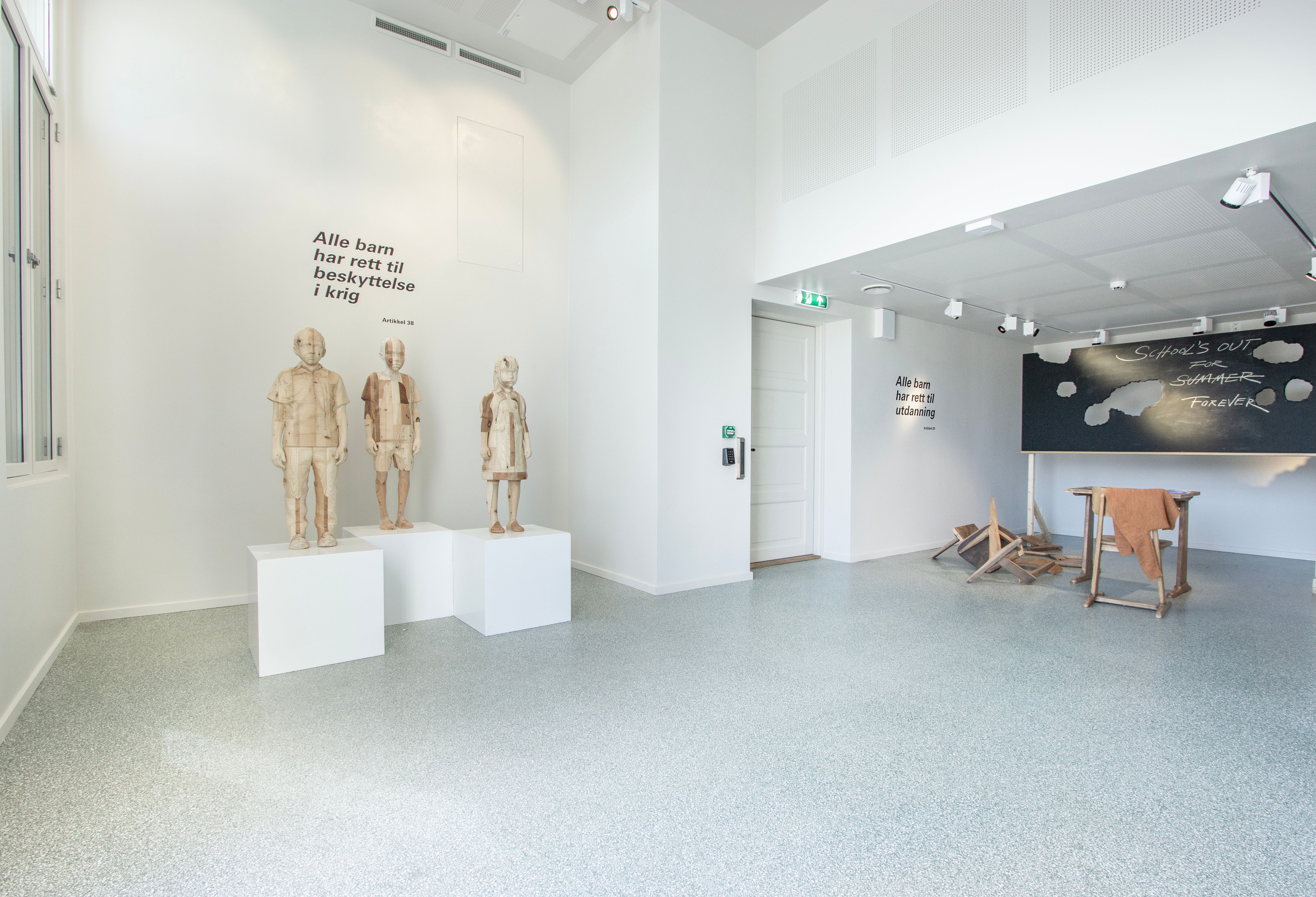 Fra utstillingen Class of No Tomorrow. Trestatuer av barn og en ødelagt skoletavle.