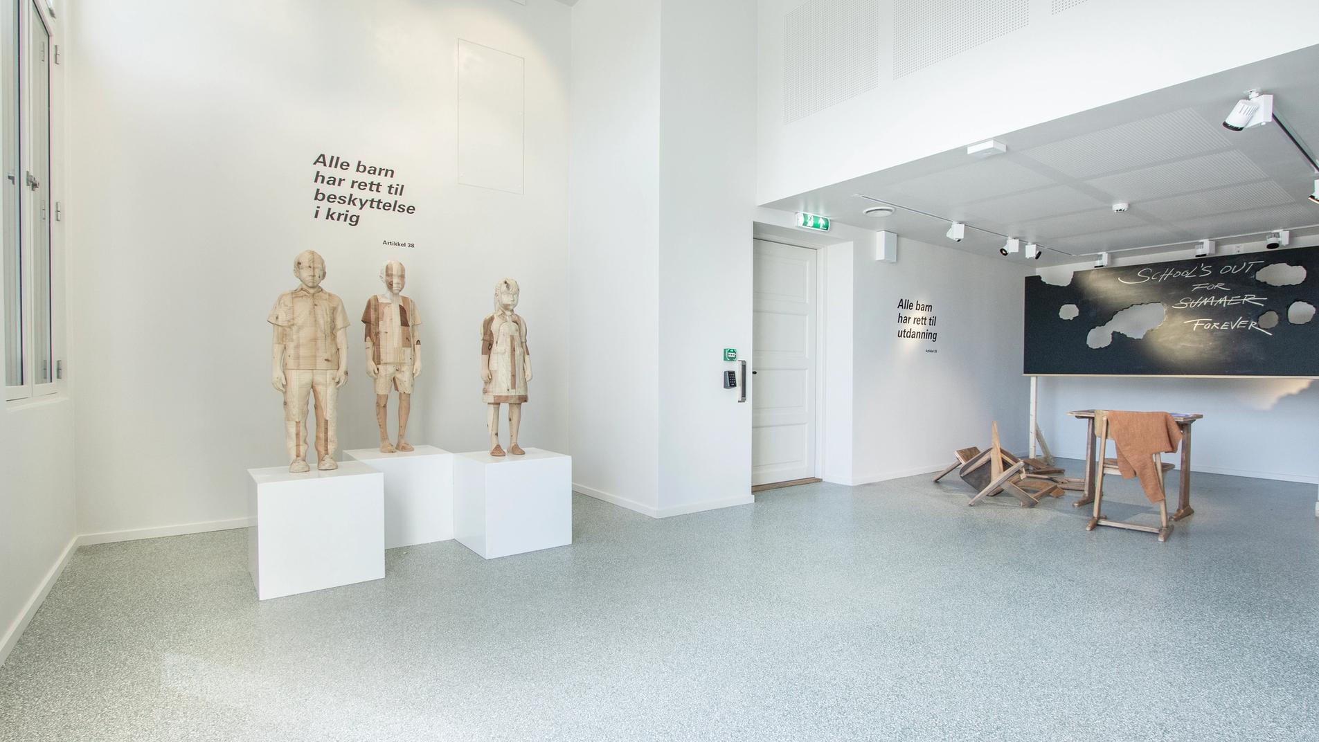 Fra utstillingen Class of No Tomorrow. Trestatuer av barn og en ødelagt skoletavle.