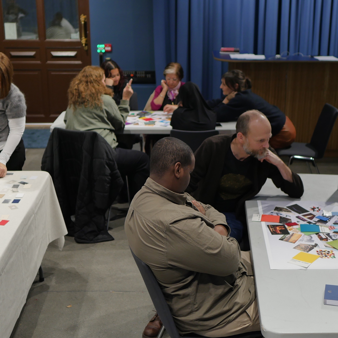 Fra workshop, folk som sitter rundt bord med bilder og farger spredt.