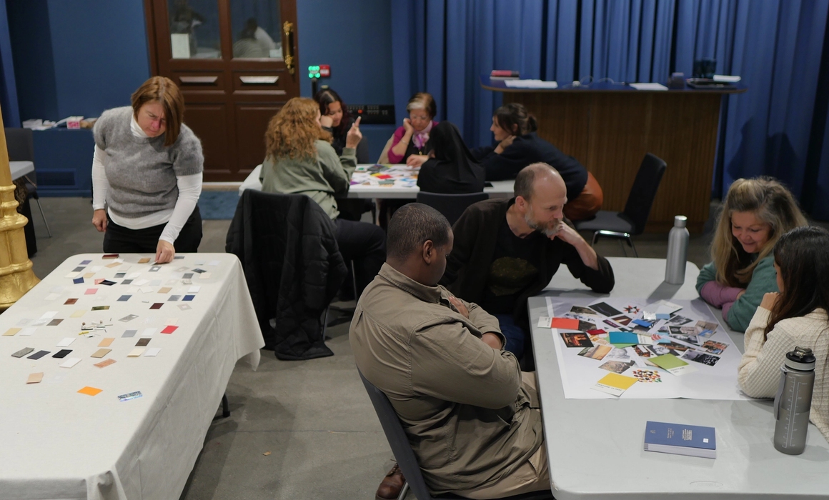 Fra workshop, folk som sitter rundt bord med bilder og farger spredt.