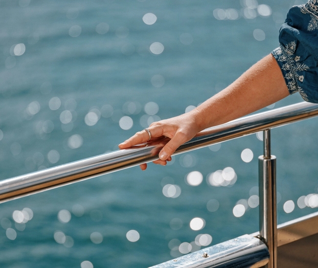 Et rekkverk med en hånd som lener seg, glitrende vann i bakgrunnen.