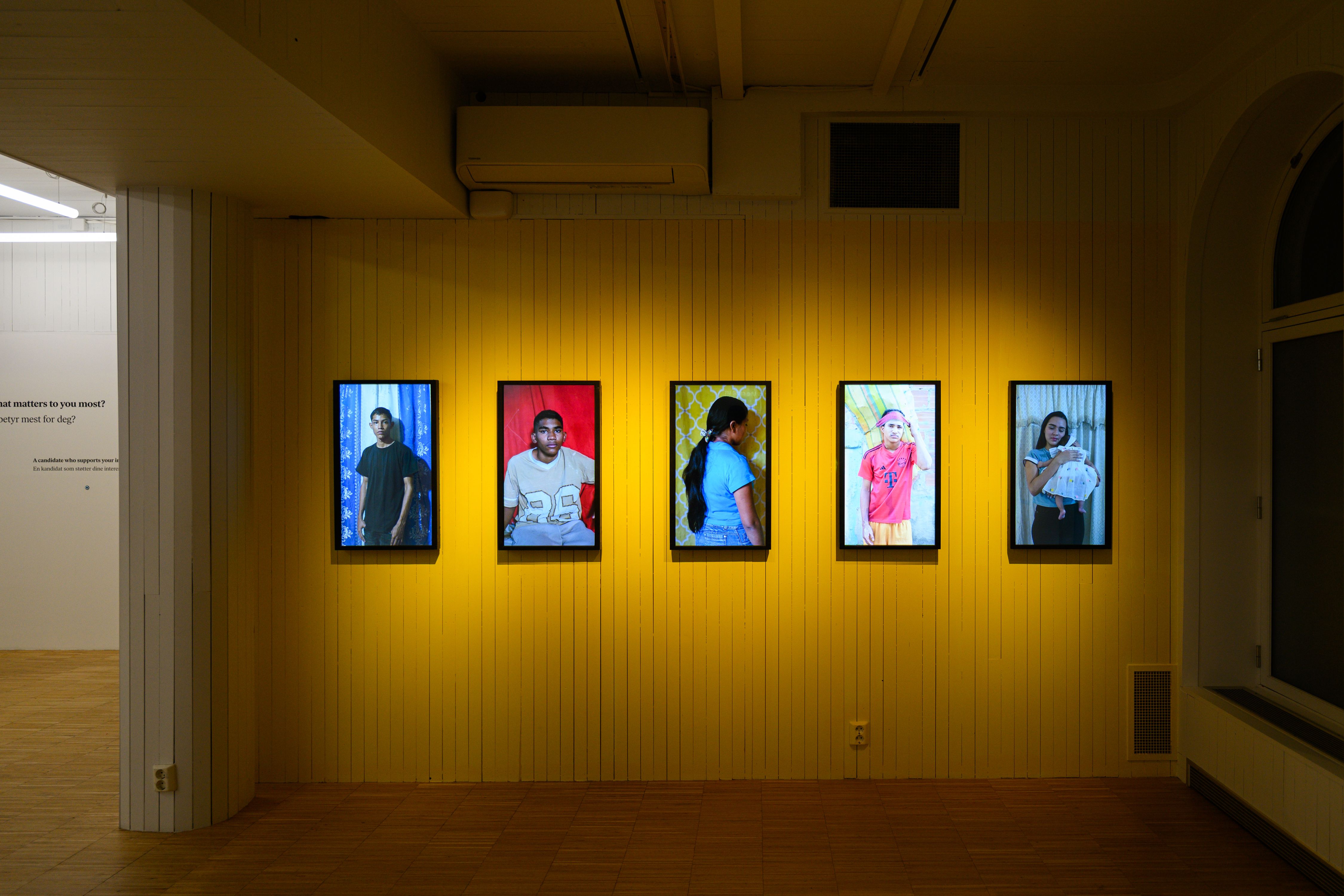 Bilde fra utstillingen, gul vegg med unge venezuelanere portretter.
