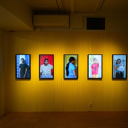 Bilde fra utstillingen, gul vegg med unge venezuelanere portretter.