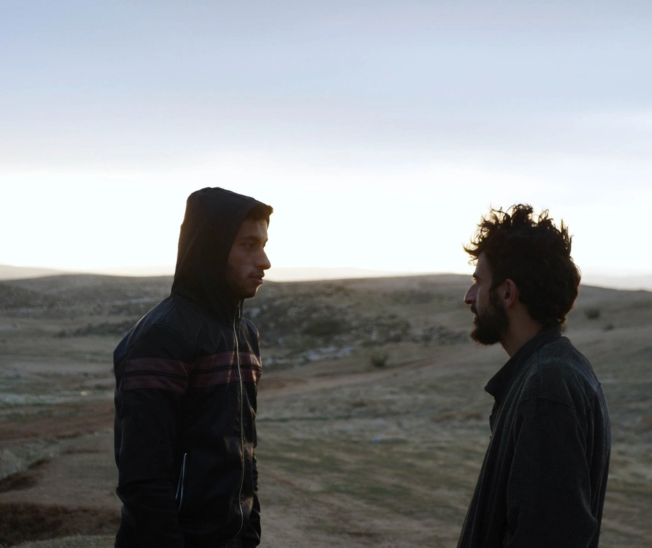 Stillbilde fra dokumentaren, de to hovedpersonene står i en ørken ved solnedgang og ser på hverandre.