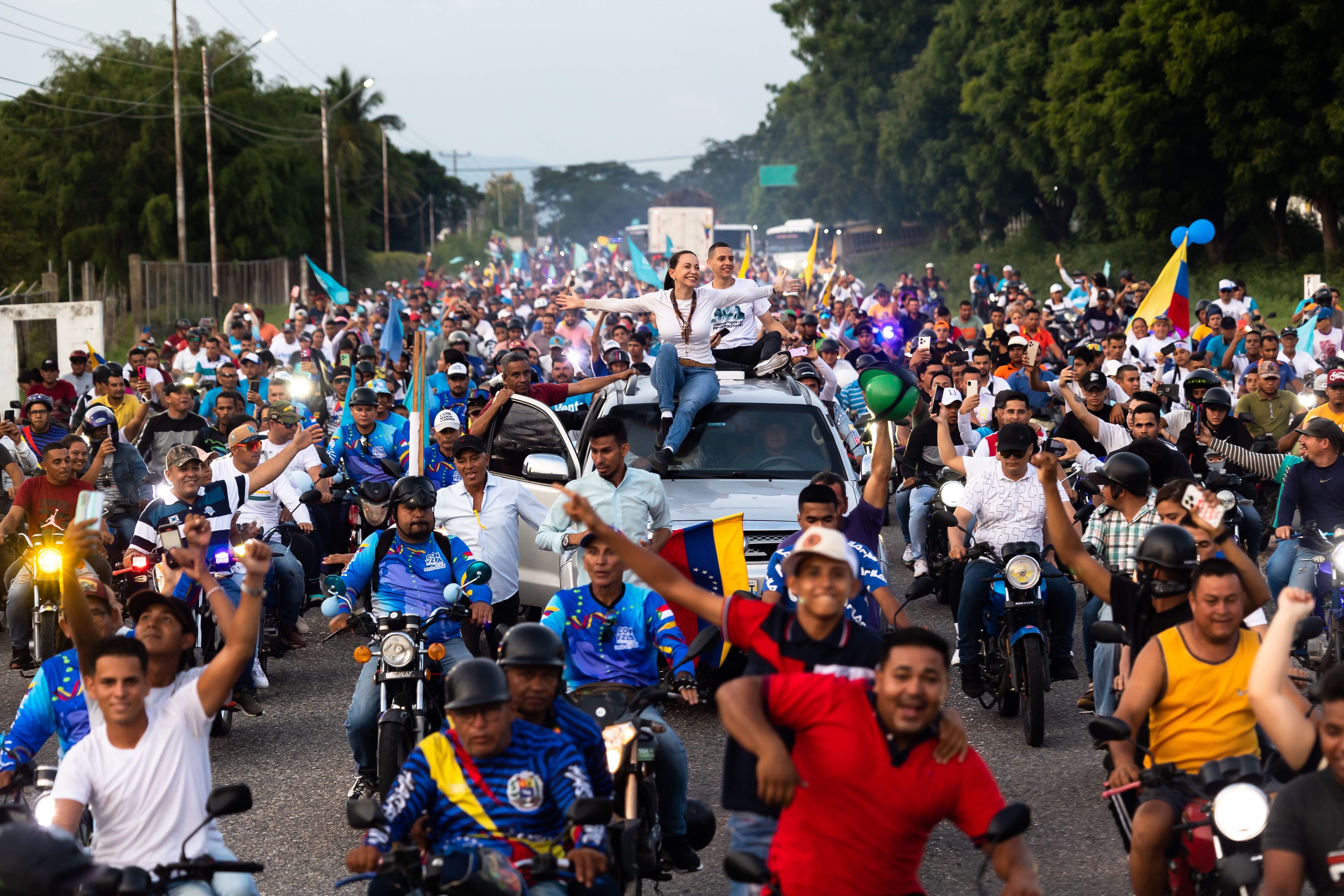Folkemengde som jubler og vaier med venezuela flagg. Støttespillere av Maria Corina, med maria corina på en bil med armene ut.