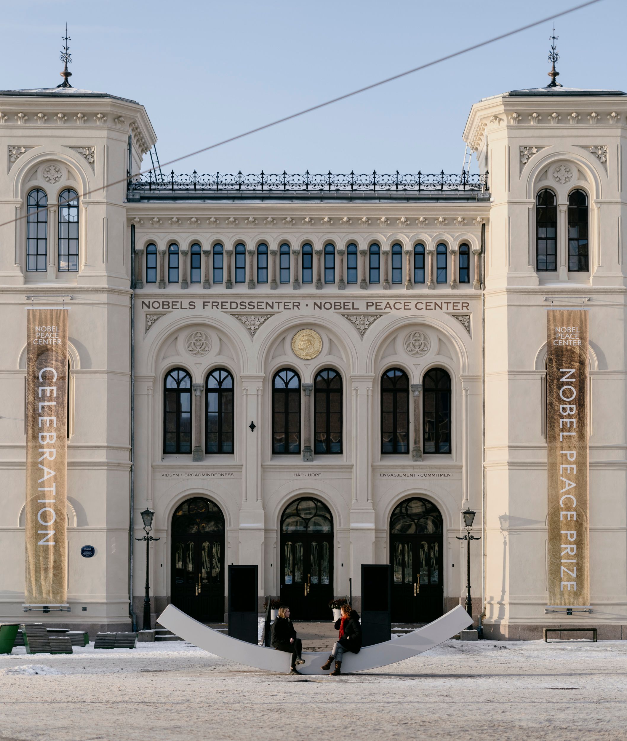 Fasaden til fredssenteret, med fredsbenken og to personer som sitter på den.