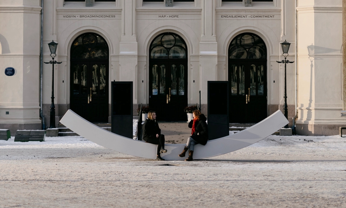 Fasaden til fredssenteret, med fredsbenken og to personer som sitter på den.