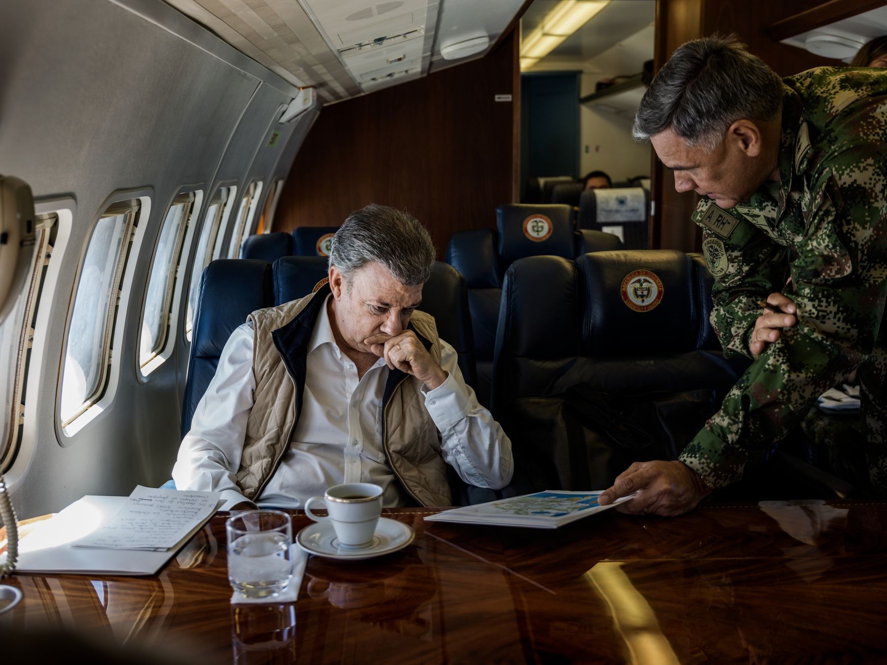 Juan Manuel santos på et fly, med millitær person som prater med han.