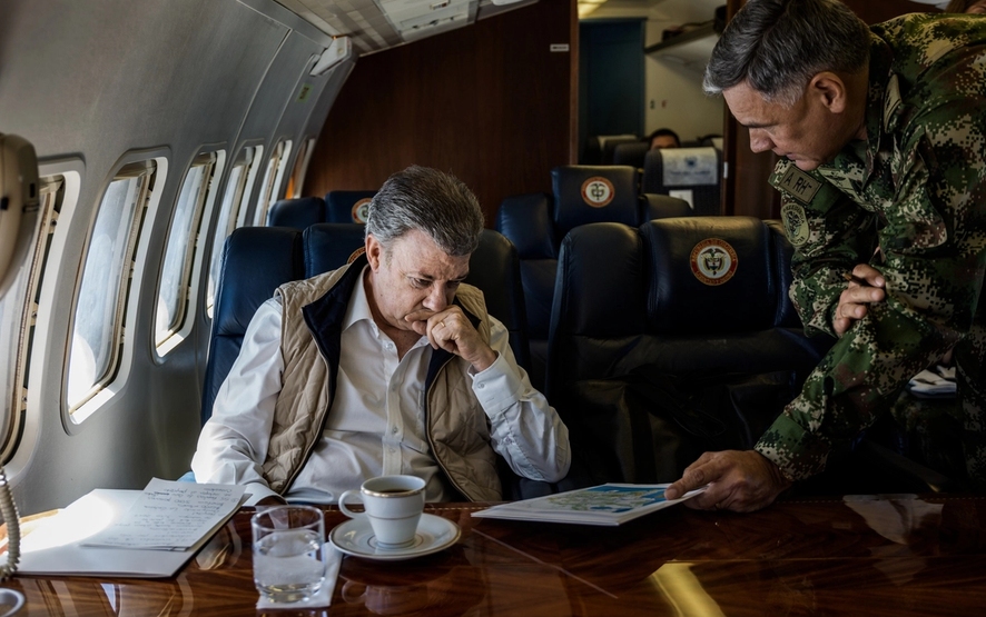 Juan Manuel santos på et fly, med millitær person som prater med han.