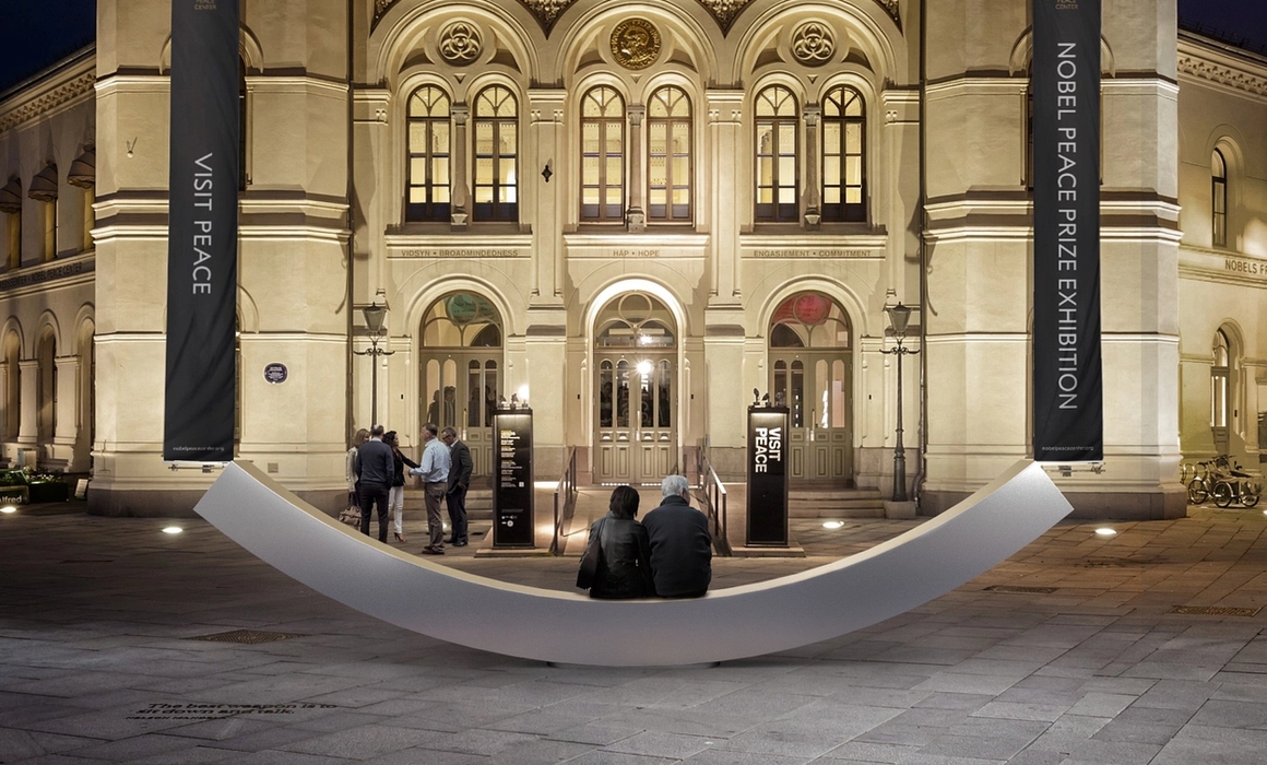 Fasaden til fredssenteret, med fredsbenken og to personer som sitter på den.