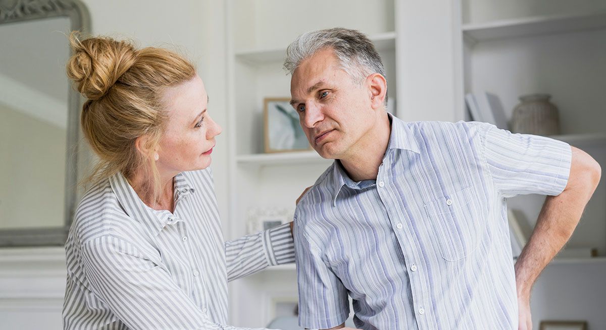 Woman supporting a man experiencing discomfort at home, illustrating the impact of chronic inflammation on daily life.