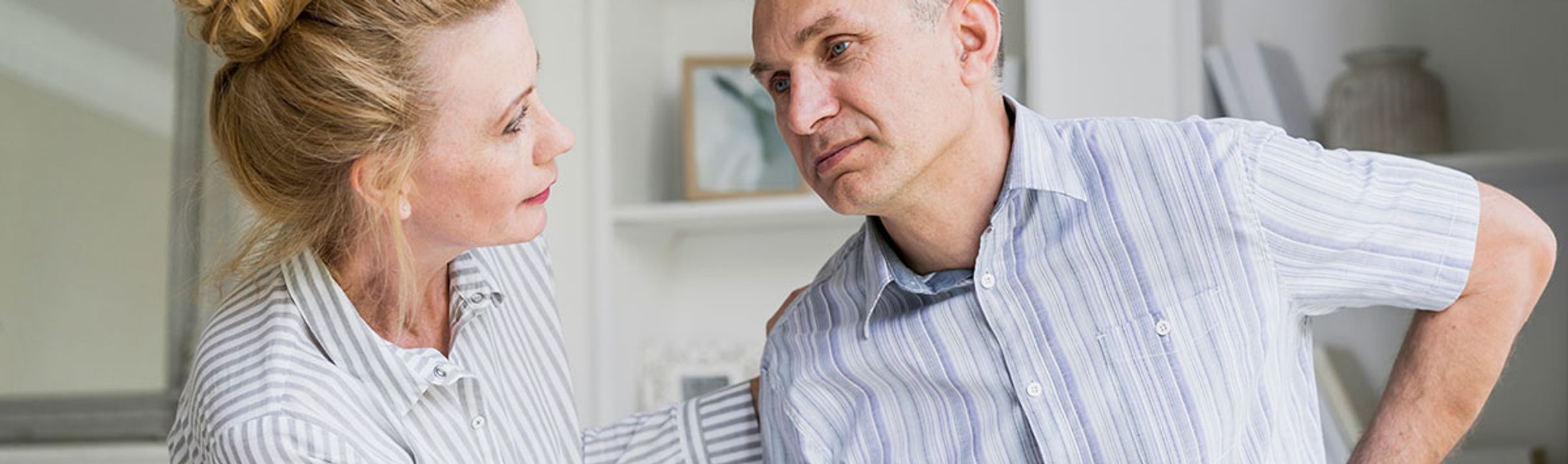 Woman supporting a man experiencing discomfort at home, illustrating the impact of chronic inflammation on daily life.