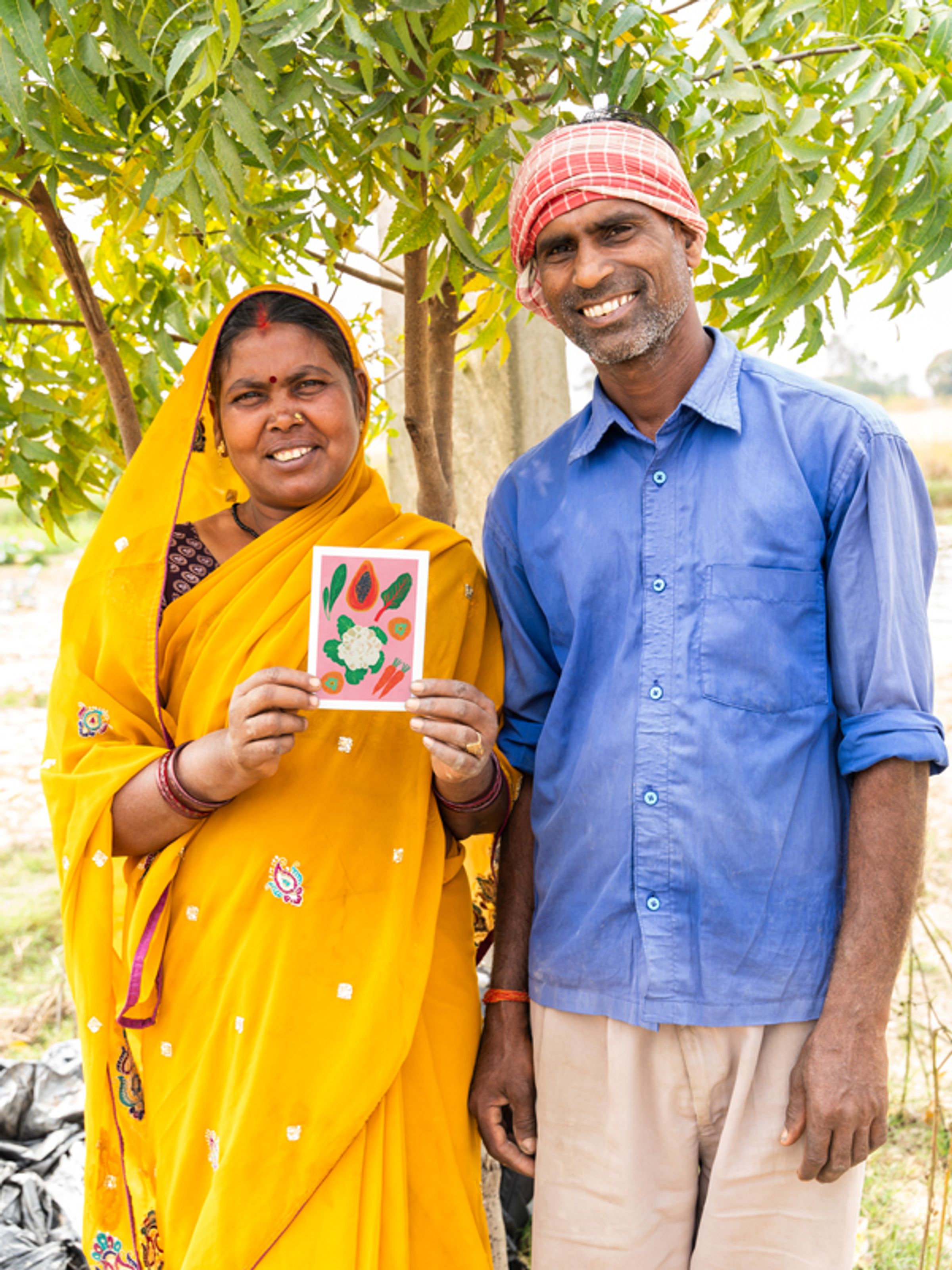 Women in red sari smiling and holding a black and white goat