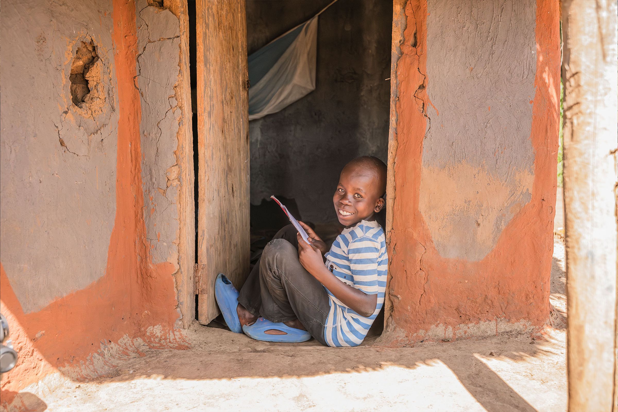 A boy smiling as he reads in the doorway of his home