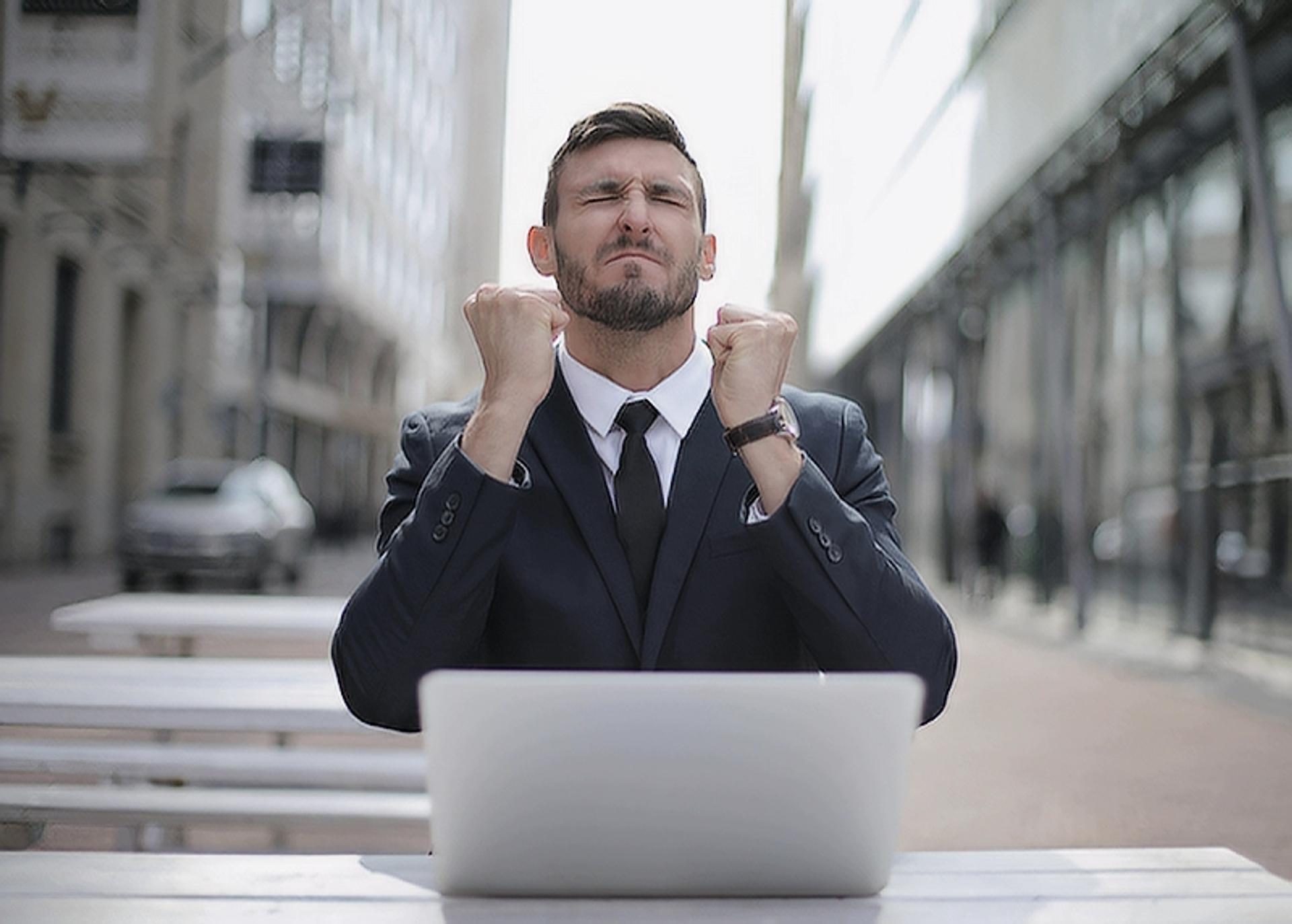 Happy and excited man sitting on bench outside with a laptop