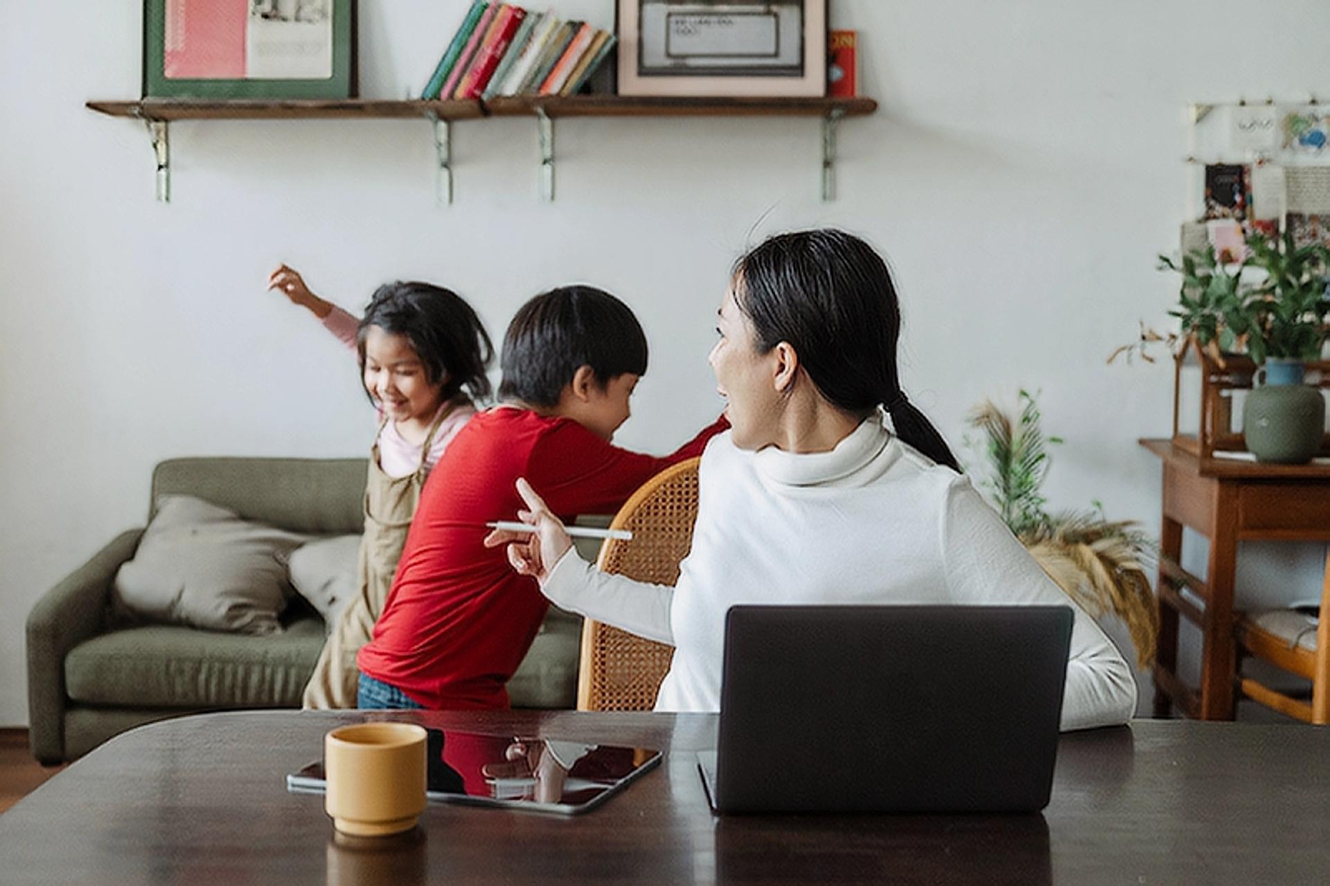 Image of mom on her computer with 2 kids behind her