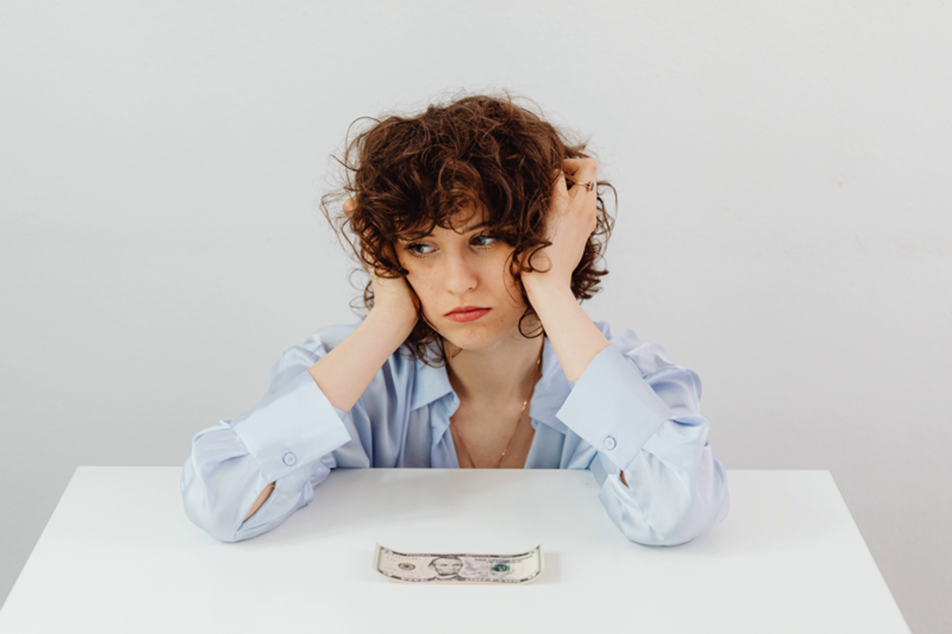Sad and stressed woman sitting at table alone with a five dollar bill in front of her