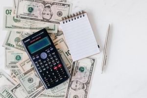 Calculator with small notebook and pen on top of spread out cash