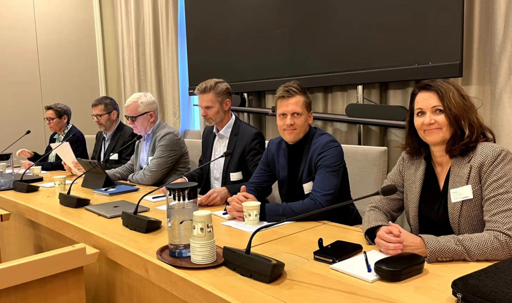 Mennesker ved et langt bord med hver sin mikrofon