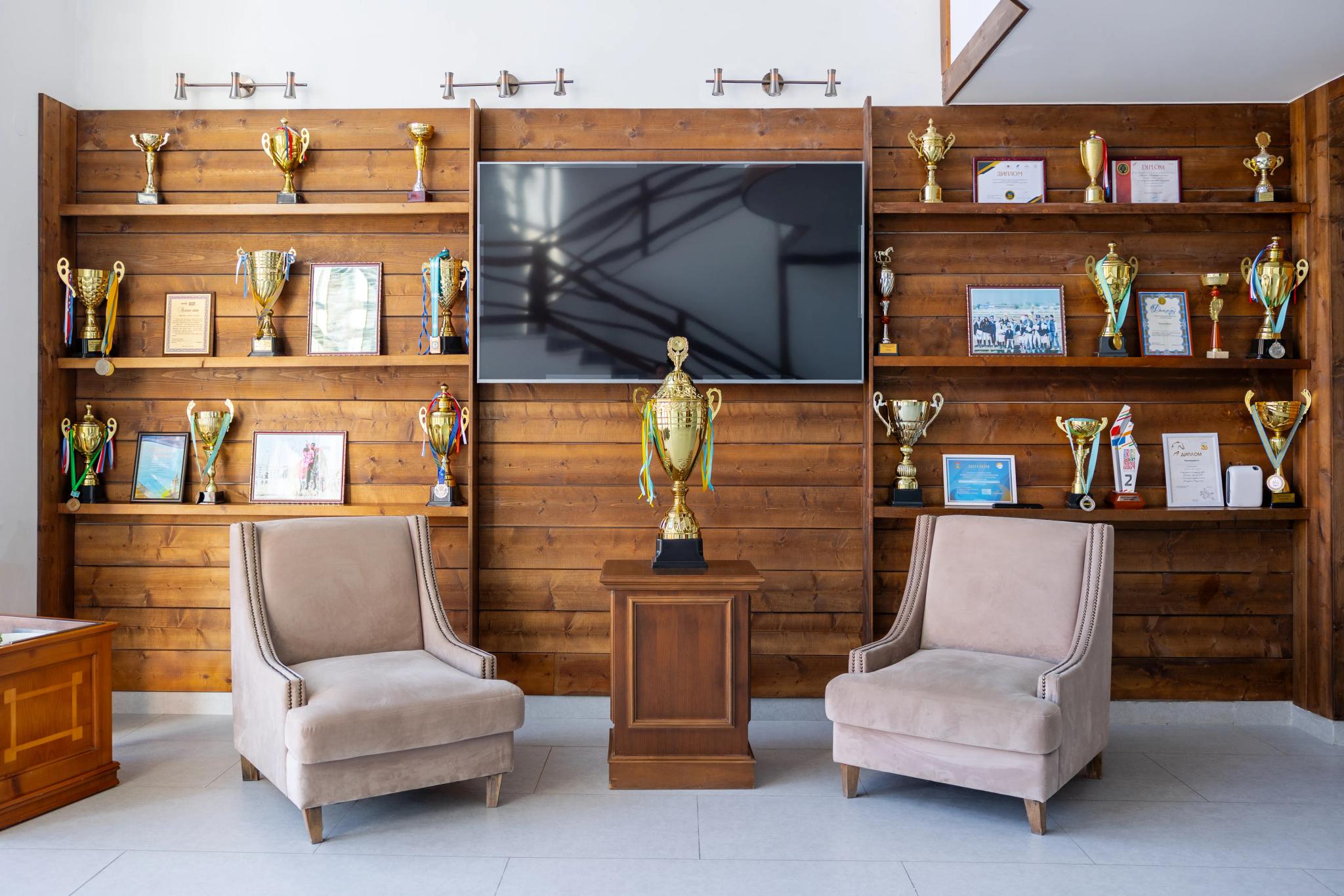 Prestige equestrian club interior in Astana: wooden shelves with trophies, TV screen and upholstered chairs. Architectural photography Kazakhstan