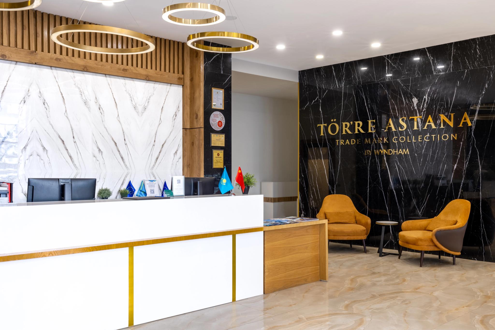 Luxury hotel lobby interior of Tor'Re Astana featuring marble accent wall, wooden reception desk and golden armchairs - professional interior photography Astana