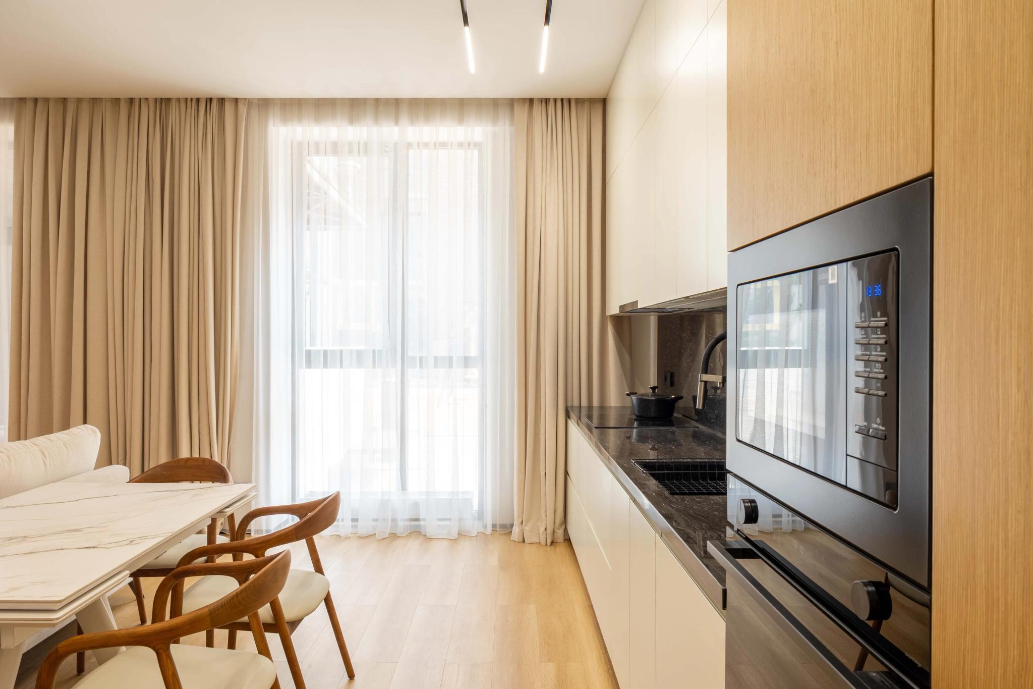 Modern studio kitchen with built-in appliances, wooden finishes and panoramic window — professional interior photography Kazakhstan