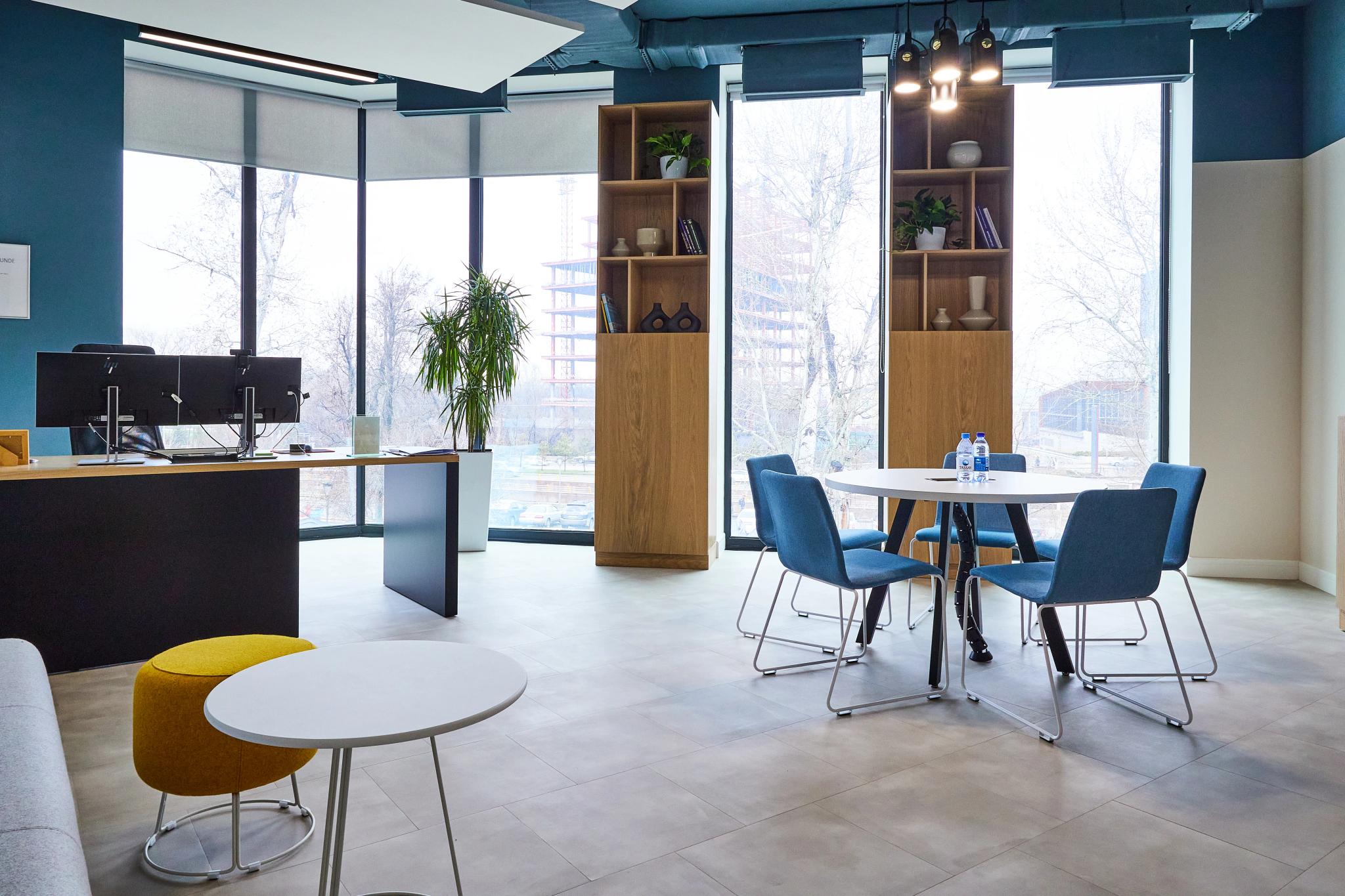 Contemporary open-space office at Esentai City Almaty featuring floor-to-ceiling windows, wooden shelving and blue accents - commercial interior photography