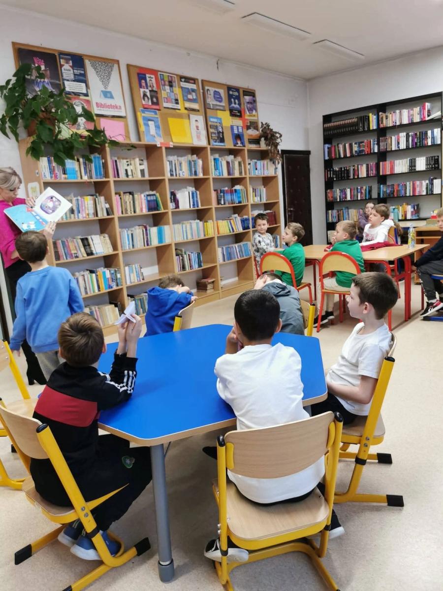 Uczniowie wsłuchują się w historię czytaną przez bibliotekarkę podczas zajęć w bibliotece.