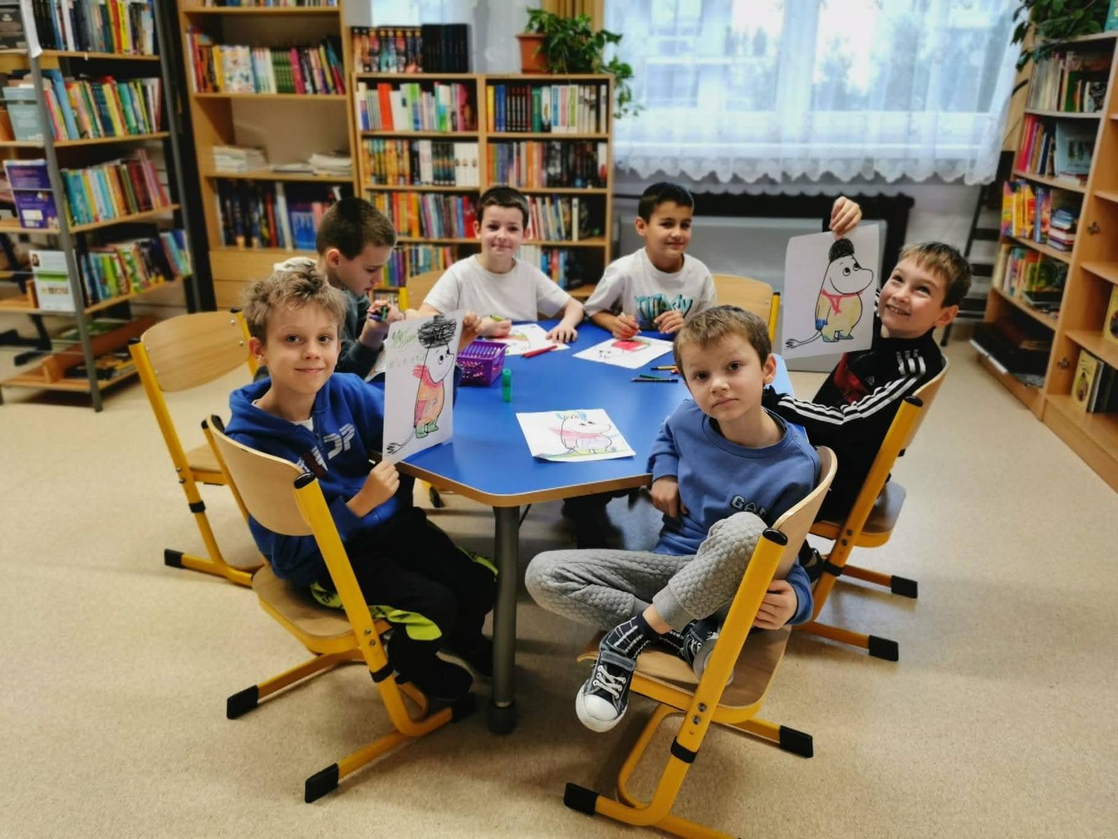Uczniowie siedzą przy stoliku i uczestniczą w zajęciach w bibliotece szkolnej.