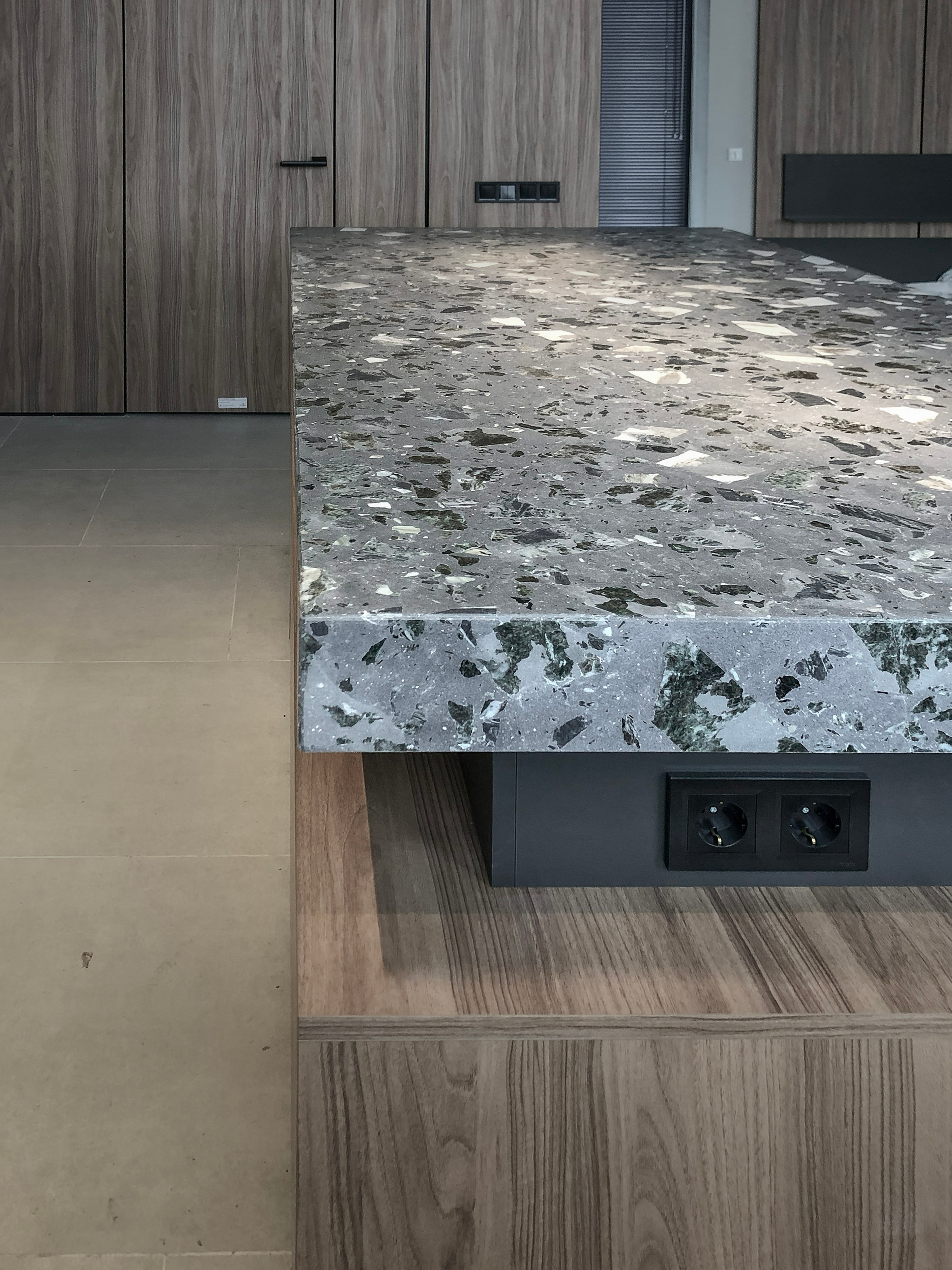 Custom terrazzo stone countertop with natural stone aggregate and integrated electrical outlets in a bespoke kitchen interior.