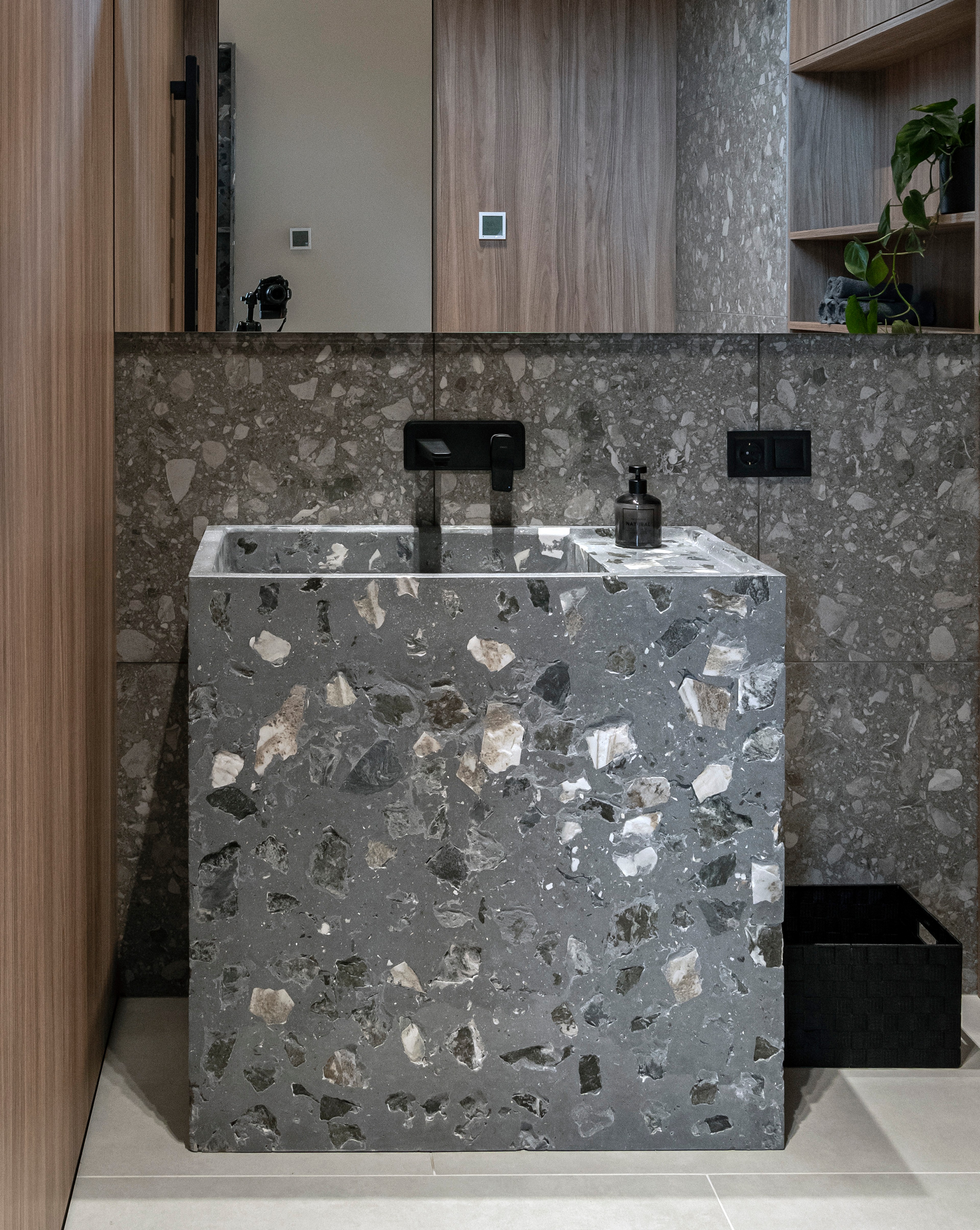 Custom monolithic terrazzo stone washbasin with natural stone aggregate and black faucet in a contemporary guest bathroom.