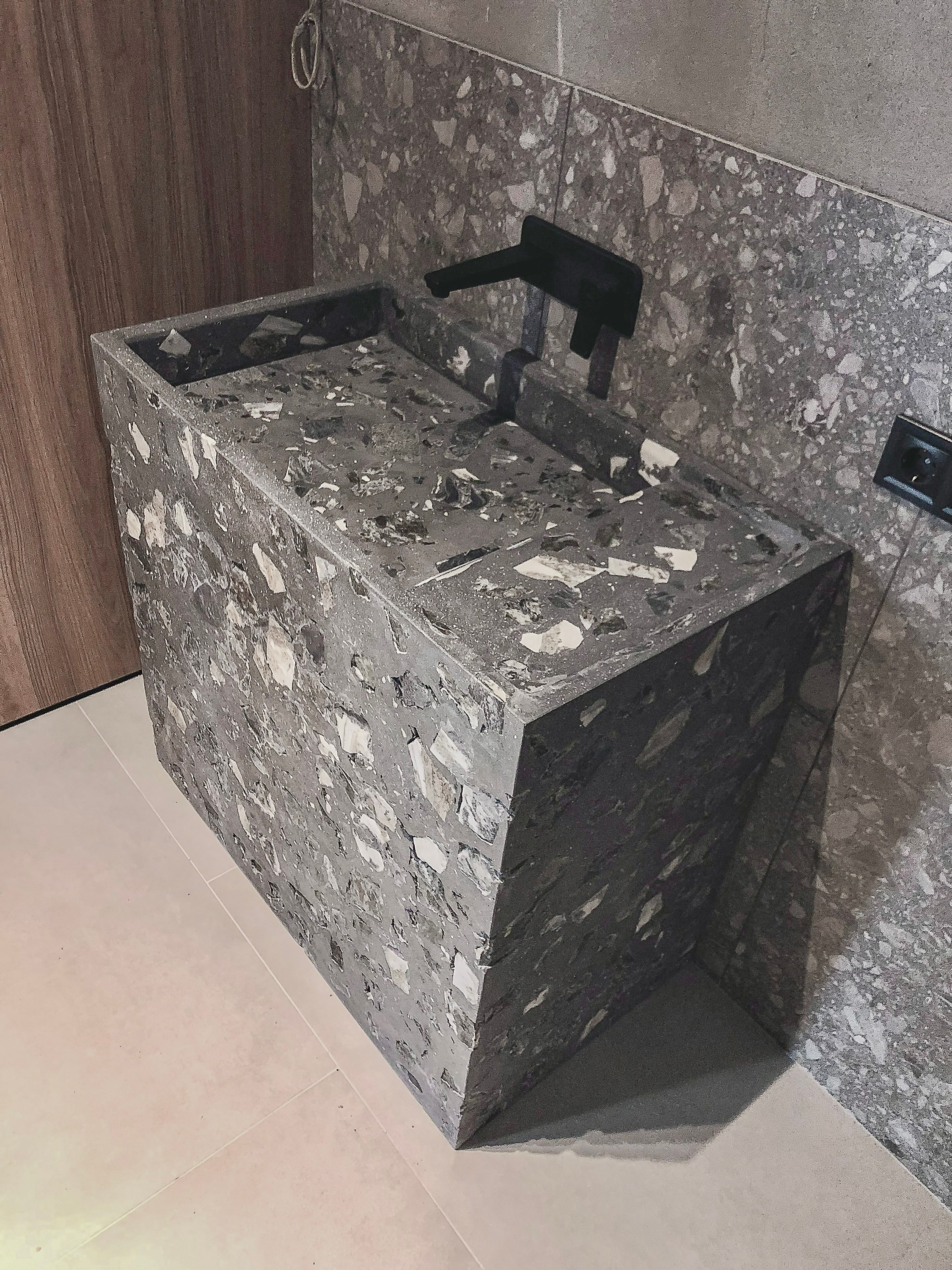 Custom monolithic terrazzo stone washbasin with natural stone aggregate and black faucet in a contemporary guest bathroom.