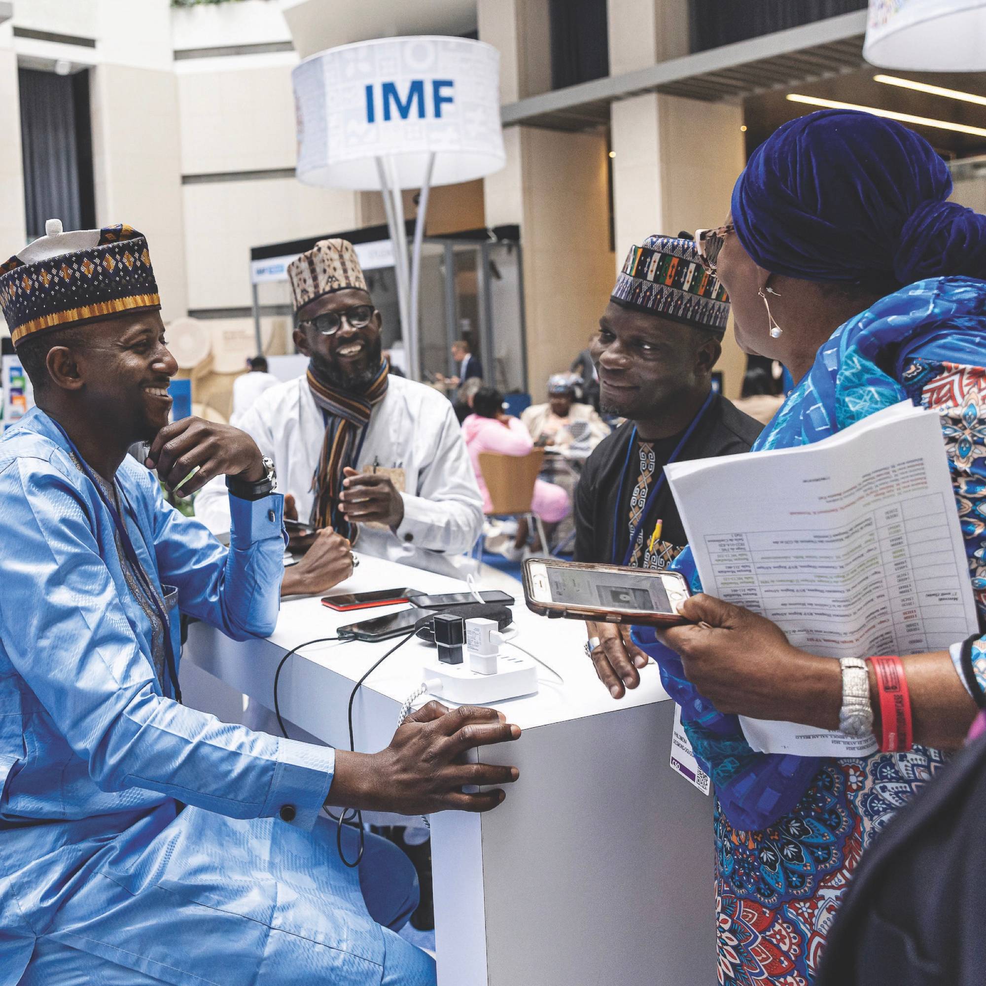 A group of people sitting and smiling as on of them charges their phone