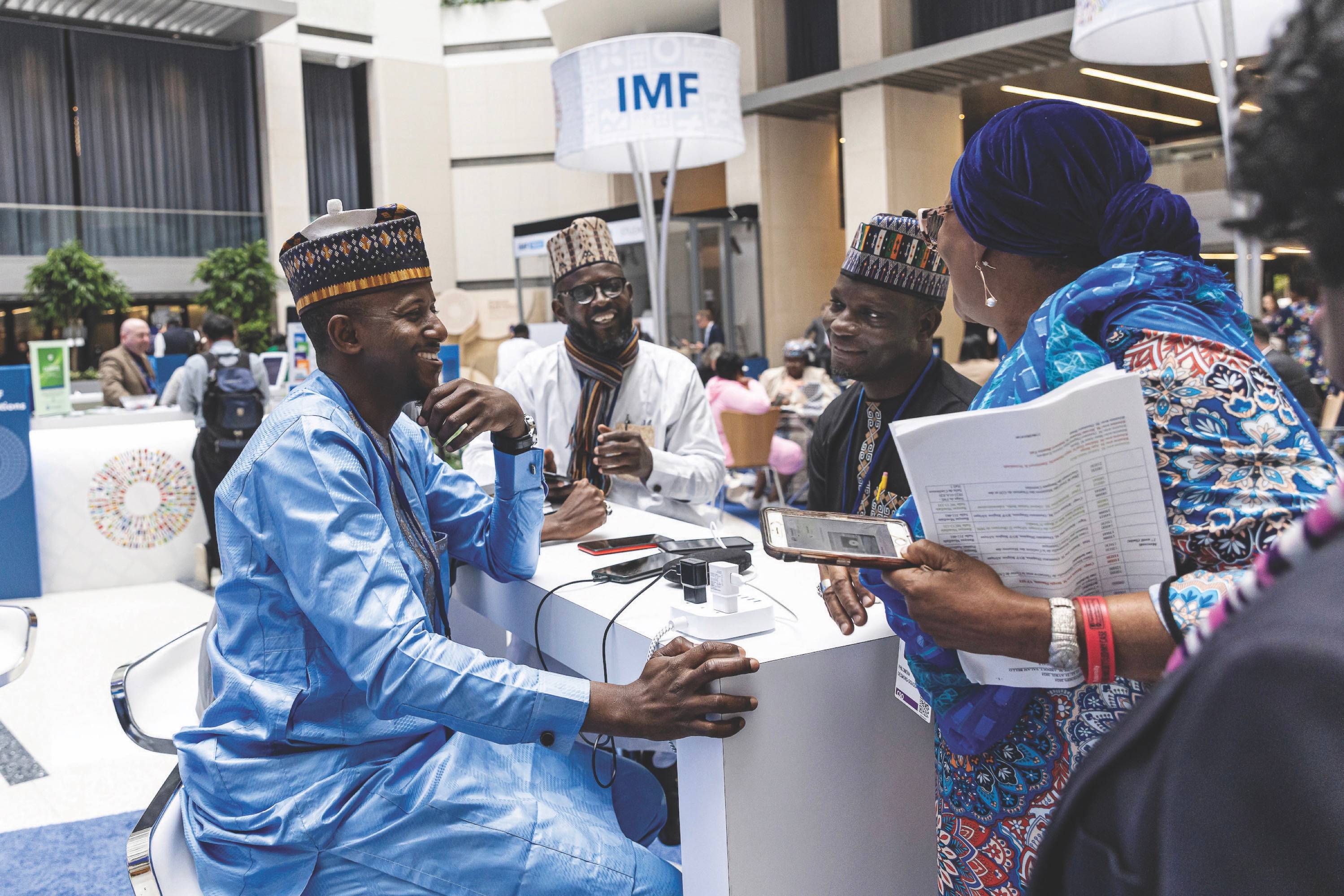A group of people sitting and smiling as on of them charges their phone
