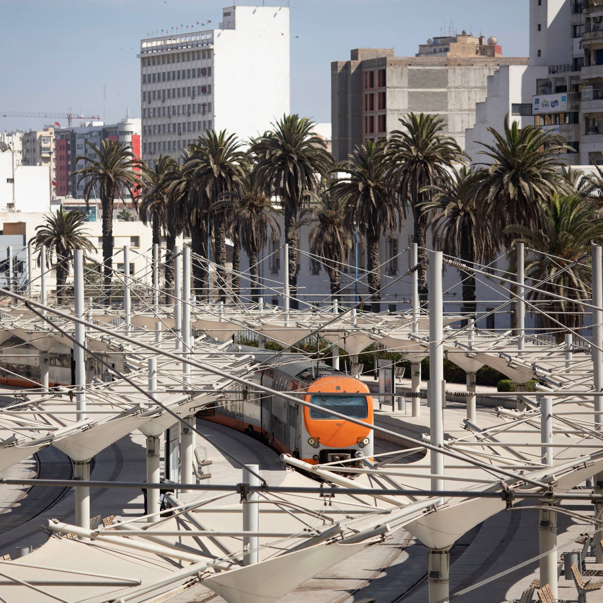 The front of a train is in view as it comes into a station with large buildings in the background.