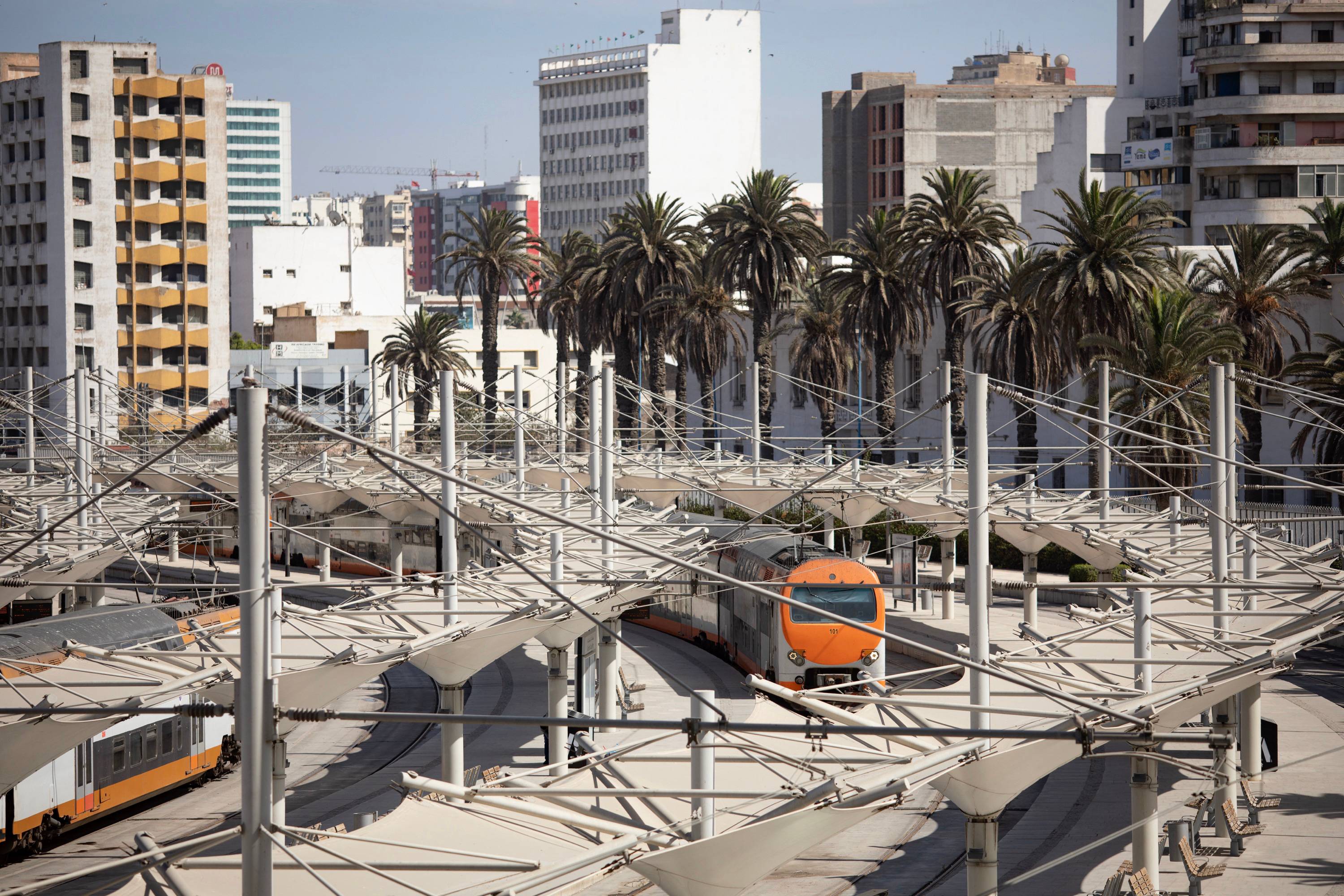 The front of a train is in view as it comes into a station with large buildings in the background.